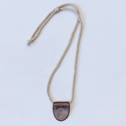 Necklace with a dark ceramic pendant on a light grey background