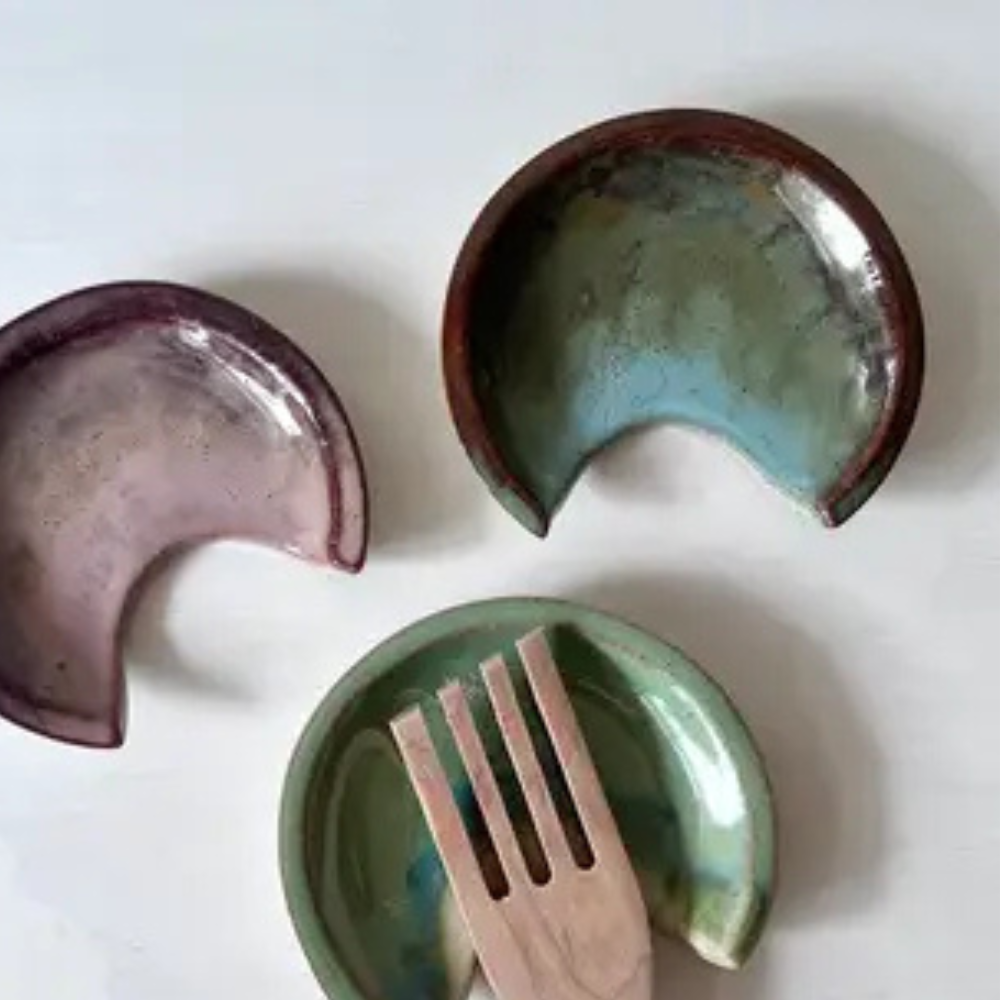 Three ceramic spoon rests with a wooden fork on a white background