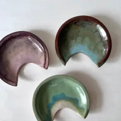Three ceramic crescent moon-shaped spoon rests in different colours on a white background