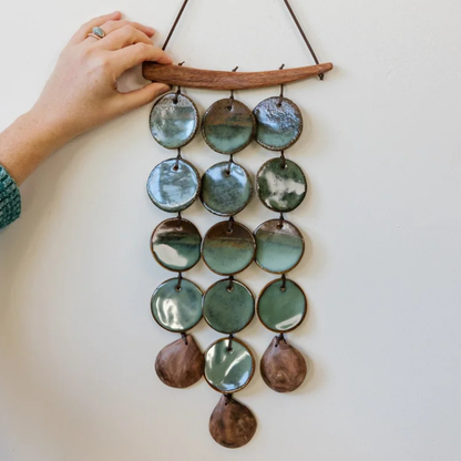 Hand holding a decorative wall hanging with ceramic discs on a plain background