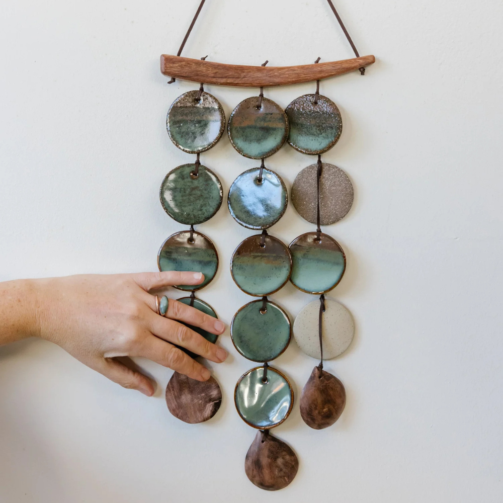 Decorative wall hanging with ceramic discs and a hand touching it on a white background