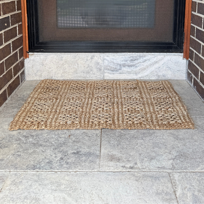 Doormat on a stone floor in front of a door with a screen